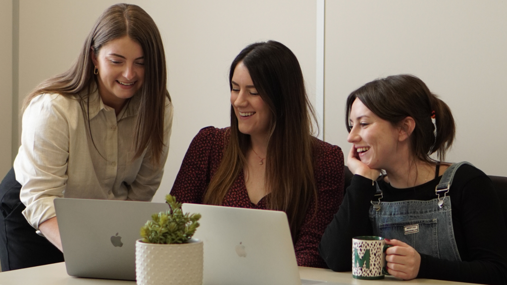 Small marketing agency team of 3 women smiling at a shared laptop screen